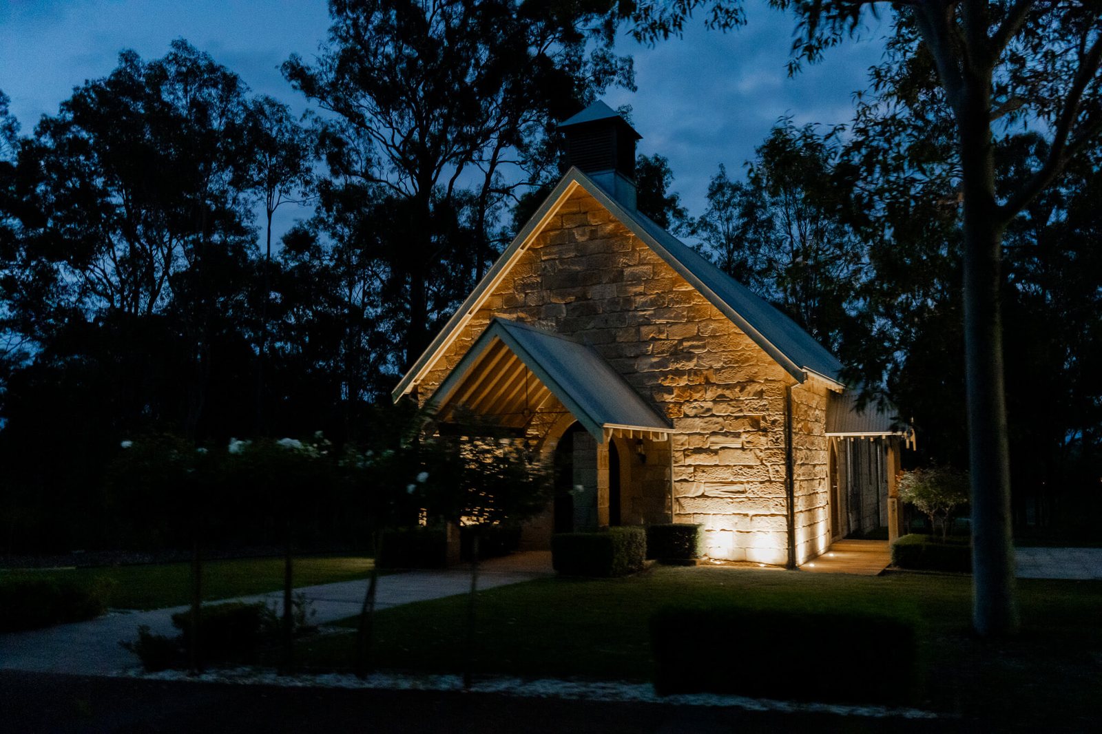 The sandstone Carriage House lit at dusk under the gum trees