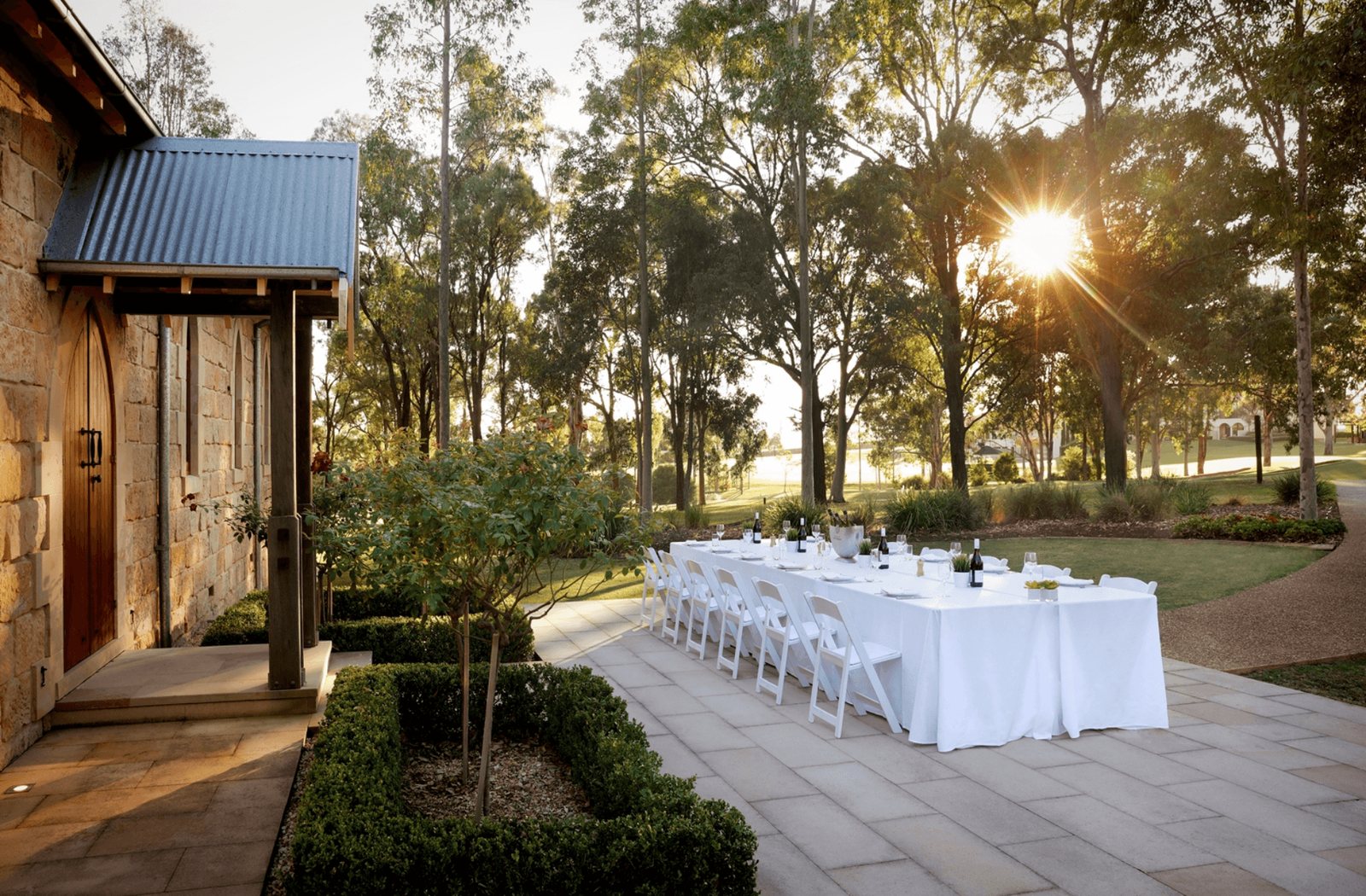 One long white table set outdoors under trees at sunset